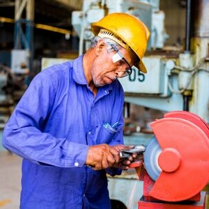 Man in yellow hard hat uses saw in a warehouse